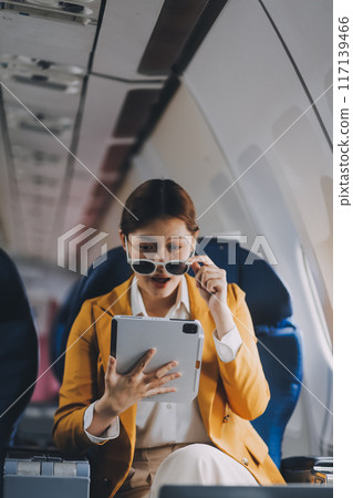A young Asian woman, seated as an airplane passenger, contemplates dollar bills, reflecting on lucrative opportunities and aspirations towards billionaire status. A young Asian woman, seated as an airplane passenger, contemplates dollar bills, reflecting on lucrative opportunities and aspirations towards billionaire status. 117139466