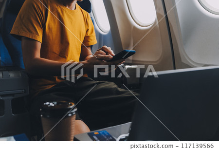 Attractive Asian businesswoman traveling on airplane playing with mobile phone while sitting in cabin. Attractive Asian businesswoman traveling on airplane playing with mobile phone while sitting in cabin. 117139566