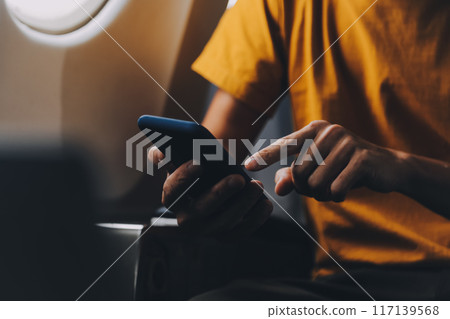 Attractive Asian businesswoman traveling on airplane playing with mobile phone while sitting in cabin. 117139568