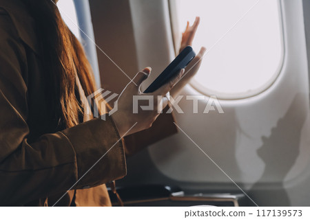 A young Asian woman, seated as an airplane passenger, contemplates dollar bills, reflecting on lucrative opportunities and aspirations towards billionaire status. 117139573
