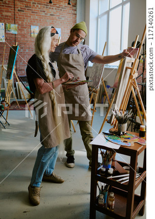 Vertical long shot of modern senior Caucasian woman having individual painting class in art studio, young teacher working with her Vertical long shot of modern senior Caucasian woman having individual painting class in art studio, young teacher working with her 117140261