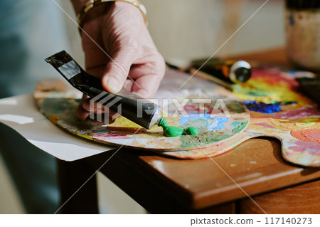 Closeup of hand of unrecognizable artist squeezing green oil paint from tube onto palette Closeup of hand of unrecognizable artist squeezing green oil paint from tube onto palette 117140273