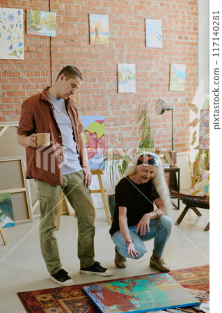 Modern senior female art teacher giving comment on abstract painting during individual class in art studio 117140281