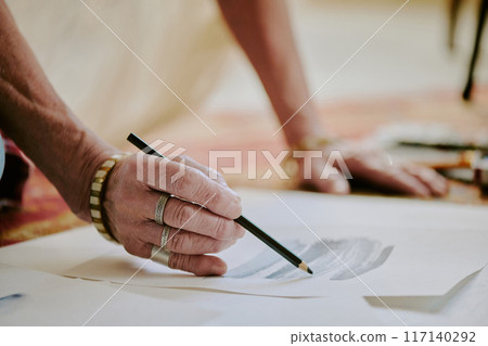 Closeup of wrinkled hand of unrecognizable senior female artist drawing pencil sketch, copy space 117140292