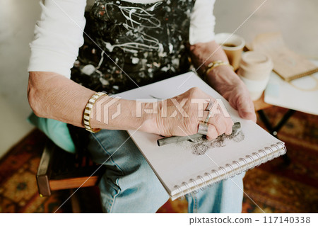 High angle view medium closeup of hands of unrecognizable elderly female artist drawing sketch with charcoal pencil 117140338