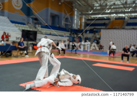 Blurred defocused image with two karate practitioners sparring on a tatami mat. 117140799