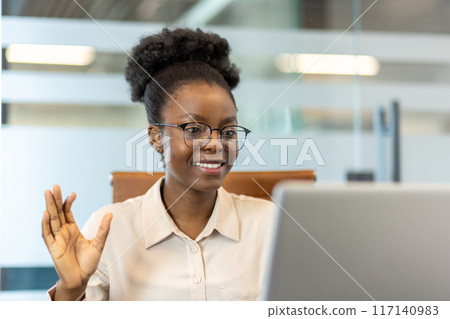 Businesswoman on video call in modern office, engaging in online meeting. Professional working remotely connecting with colleagues through virtual communication. Concept of technology, remote work 117140983