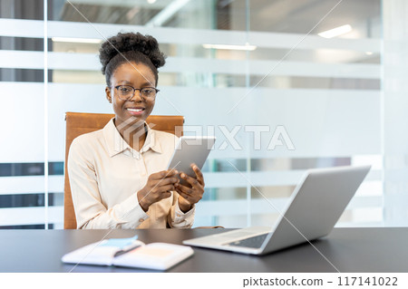 Professional businesswoman using tablet in modern office with laptop and notebook. Confident and productive at work. Achieving goals with technology, workspace Professional businesswoman using tablet in modern office with laptop and notebook. Confident and productive at work. Achieving goals with technology, workspace 117141022