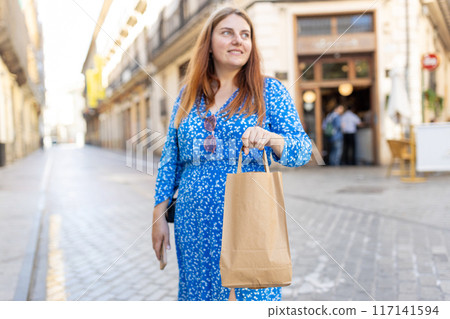 Happy 30s woman holding paper shopping bag on old town background. Zero waste concept. Eco Nature Friendly Style. Environmental Conservation Recycling mock up 117141594