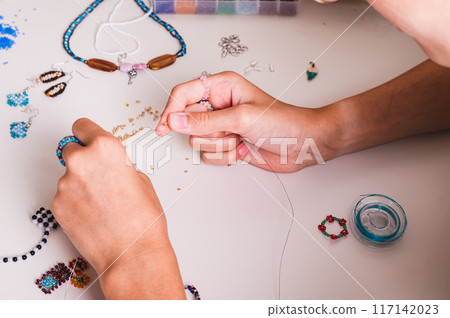 Girl doing beadwork on work table with beads and wire 117142023