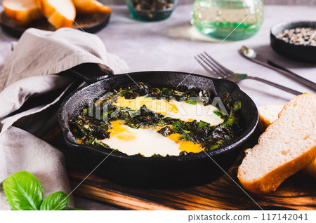 Green shakshuka with basil and green onions in a frying pan on the table 117142041