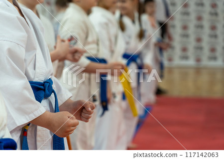 A close-up of a row of children in white karate kimonos with clenched fists. A close-up of a row of children in white karate kimonos with clenched fists. 117142063
