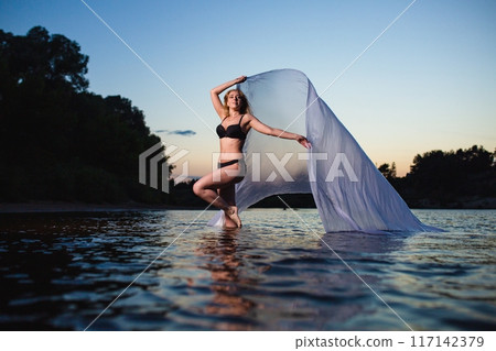 Young girl posing in the water with big piece of white fabric Young girl posing in the water with big piece of white fabric 117142379