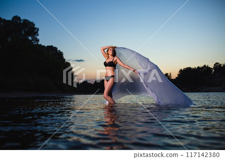 Young girl posing in the water with big piece of white fabric Young girl posing in the water with big piece of white fabric 117142380