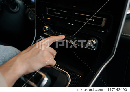 Closeup cropped shot of unrecognizable driver male pressing emergency stop button in car. Closeup of man finger pressing emergency button on car dashboard. Using emergency lights when car breaks down. Closeup cropped shot of unrecognizable driver male pressing emergency stop button in car. Closeup of man finger pressing emergency button on car dashboard. Using emergency lights when car breaks down. 117142490