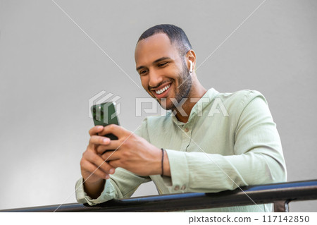 Young black man walking in city holding phone using online application outdoors. 117142850