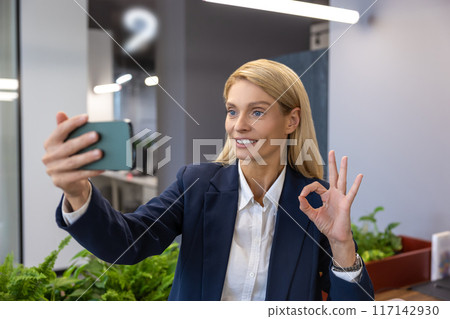 Smiling businesswoman on video call with colleague showing ok sign 117142930