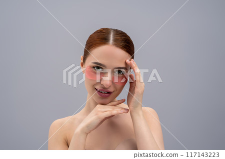 Cute young woman using beauty patches under her eyes and looking contented Cute young woman using beauty patches under her eyes and looking contented 117143223