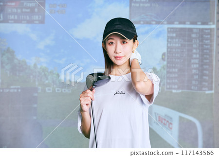 A woman practicing at an indoor golf driving range 117143566