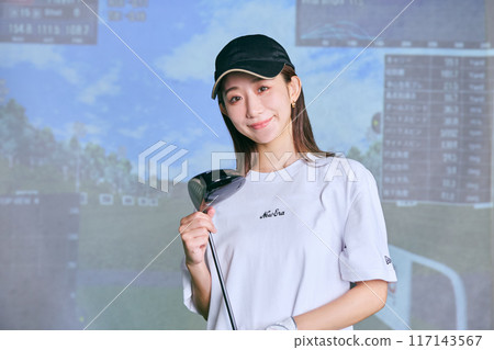 A woman practicing at an indoor golf driving range 117143567