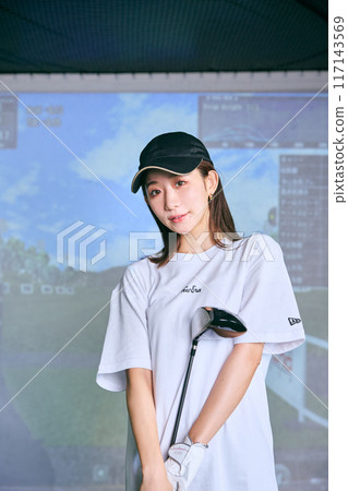 A woman practicing at an indoor golf driving range 117143569