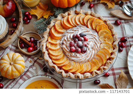 Pumpkin pie with cream and berry. Autumn dinner with cake dessert. Food for fall holidays, Thanksgiving, Halloween. Cream tart dish top view. Autumn table background with cinnamon, cranberry, pumpkin 117143701