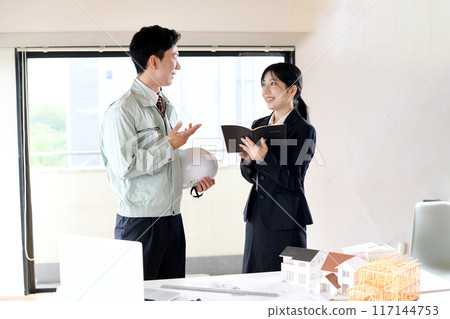 Male and female office workers discussing in front of a construction model 117144753