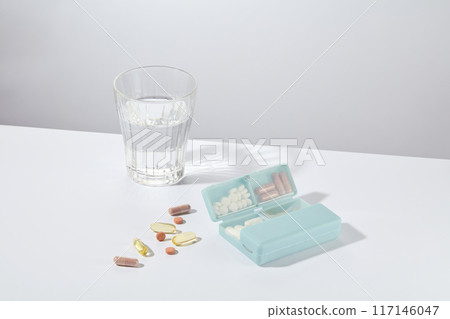 High angle shot at a white table top, which displaying some items for medicine drinking consist of a glass of water, pill box and variety vitamin supplements. Empty space for designing 117146047