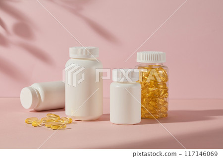 Pink background features some white blank label bottle of medicine and a fish oil supplement bottle, flat lay yellow capsules. Photo of front angle, copy space for adding text Pink background features some white blank label bottle of medicine and a fish oil supplement bottle, flat lay yellow capsules. Photo of front angle, copy space for adding text 117146069