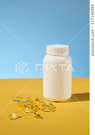 Mockup of white vitamin supplements jar without label displayed on yellow countertop, several soft yellow capsules flat lay beside. Blue background, front angle shot 117146084