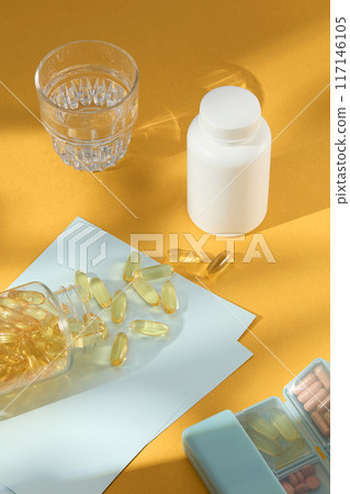 Photo for advertising vitamins and minerals supplement product, which is need to survive, grow and work. Blank label mock up bottle, glass of water, pill box, scattered lay yellow capsules Photo for advertising vitamins and minerals supplement product, which is need to survive, grow and work. Blank label mock up bottle, glass of water, pill box, scattered lay yellow capsules 117146105