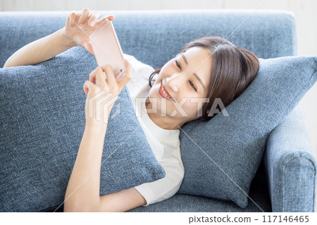 A woman lying on the sofa looking at her smartphone 117146465