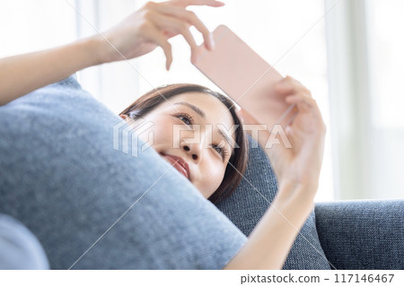 一個女人躺在沙發上看著她的智慧型手機 117146467