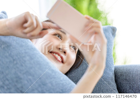 A woman lying on the sofa looking at her smartphone 117146470