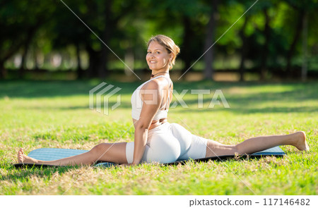 Fit girl performing front split in summer park 117146482