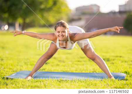 Girl in park on green grass of lawn performs Himavanasana 117146502