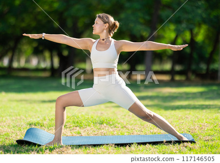 Girl in park on green grass of lawn performs padmasana 117146505