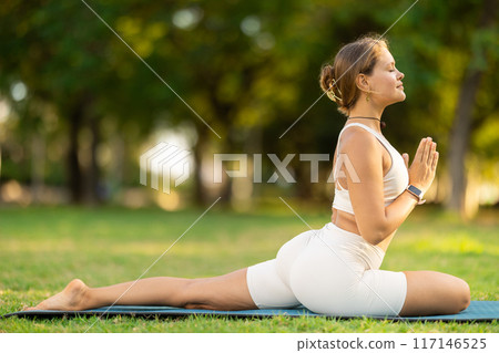 Sporty girl performing yoga asanas on green meadow in summer Sporty girl performing yoga asanas on green meadow in summer 117146525