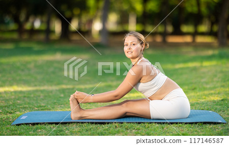 Sporty girl performing yoga asanas on green meadow in summer 117146587