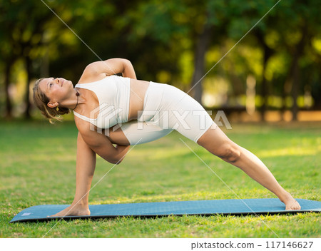 Young woman performing Baddha Parsvakonasana on green meadow Young woman performing Baddha Parsvakonasana on green meadow 117146627