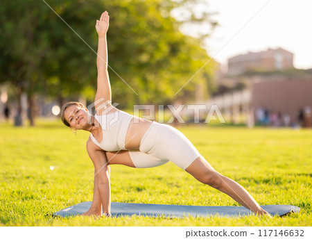 Girl doing Utthita Parsvakonasana during yoga workout on green meadow Girl doing Utthita Parsvakonasana during yoga workout on green meadow 117146632