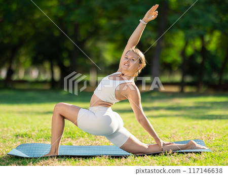 Girl in park on green grass of lawn performs Anjaneyasana 117146638