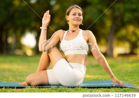 Girl performing Lord of Fishes yoga pose in summer park 117146639