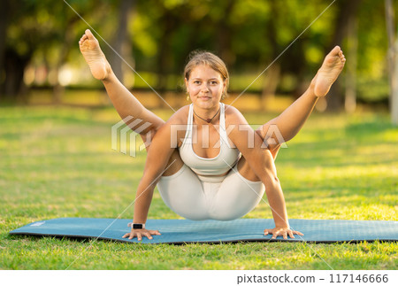 Girl in park on green grass of lawn performs Bhujapidasana 117146666