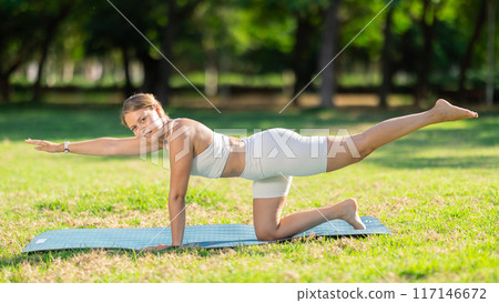 Fit girl performing balancing table yoga pose on green meadow 117146672