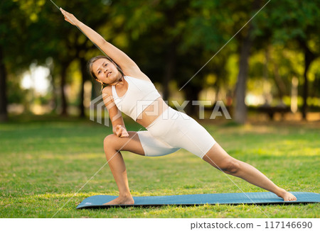 Girl in park on green grass of lawn performs Utthita Parshvakonasana Girl in park on green grass of lawn performs Utthita Parshvakonasana 117146690
