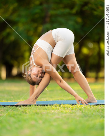 Girl in park on green grass of lawn performs Parshvottanasana 117146692