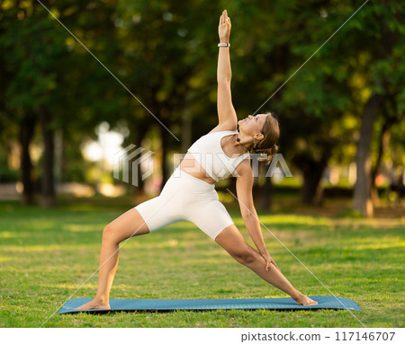 Girl performing Reverse Warrior pose during yoga routine in summer park Girl performing Reverse Warrior pose during yoga routine in summer park 117146707
