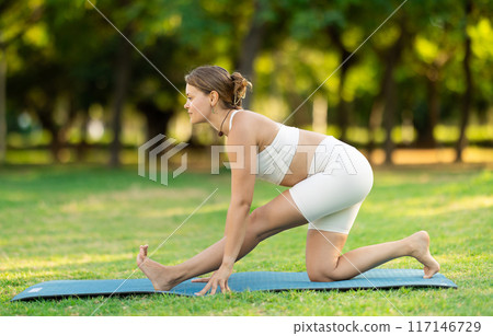 Girl in park on green grass of lawn performs hatha yoga Girl in park on green grass of lawn performs hatha yoga 117146729