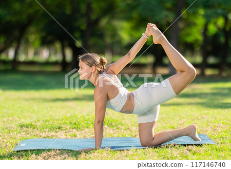 Young girl performing tiger pose during yoga session in summer park 117146740